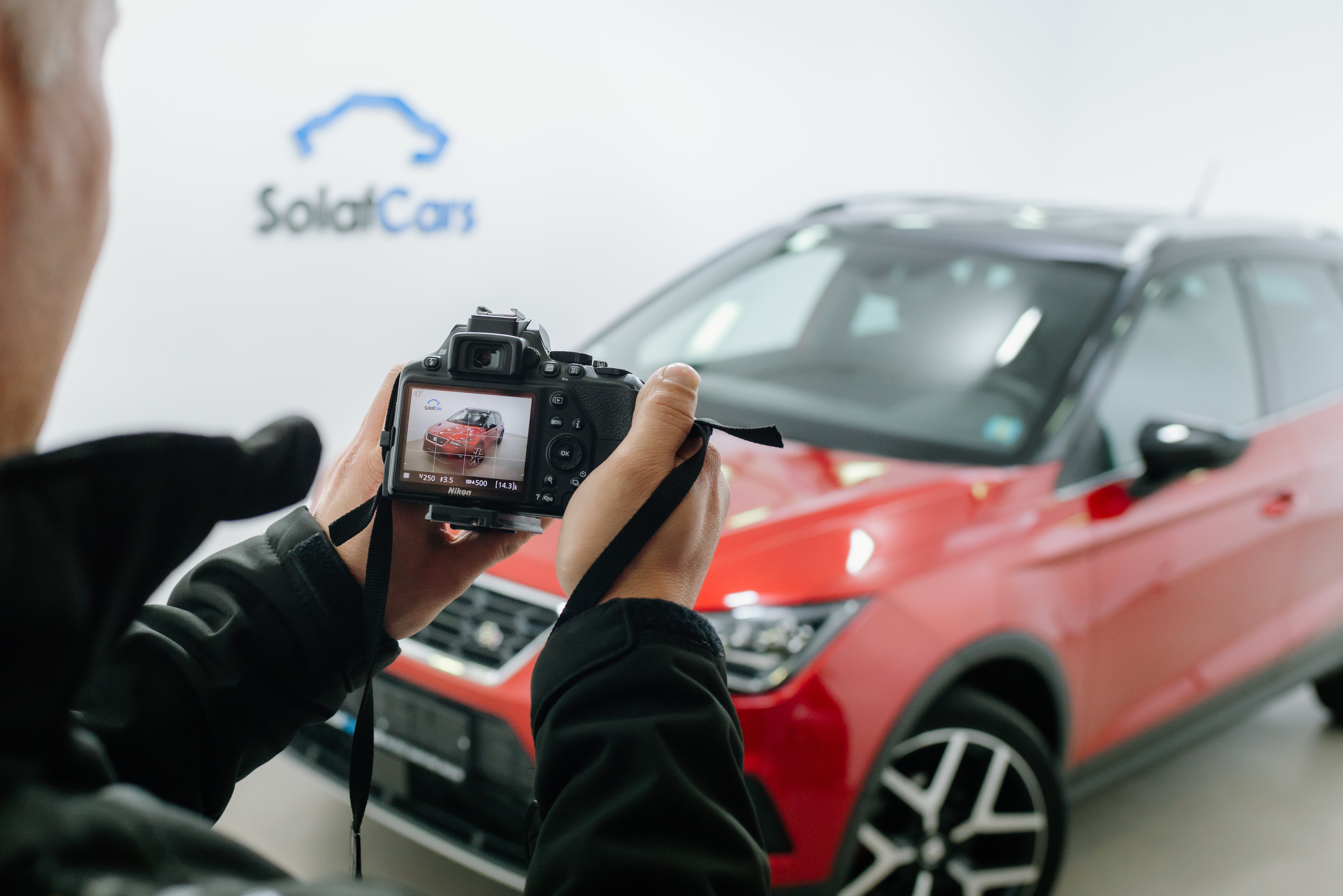 Nahaufnahme eines Mannes, der mit einer DSLR-Kamera ein rotes Auto in einem Fotostudio fotografiert